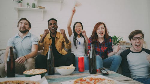 Friends cheering together during a game day party with pizza and snacks