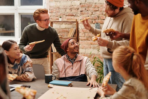 Large group of people enjoying pizza together with empty pizza boxes on the table