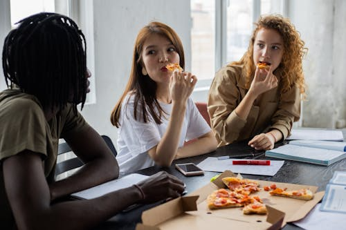 Office employees eating pizza while discussing work during a team lunch