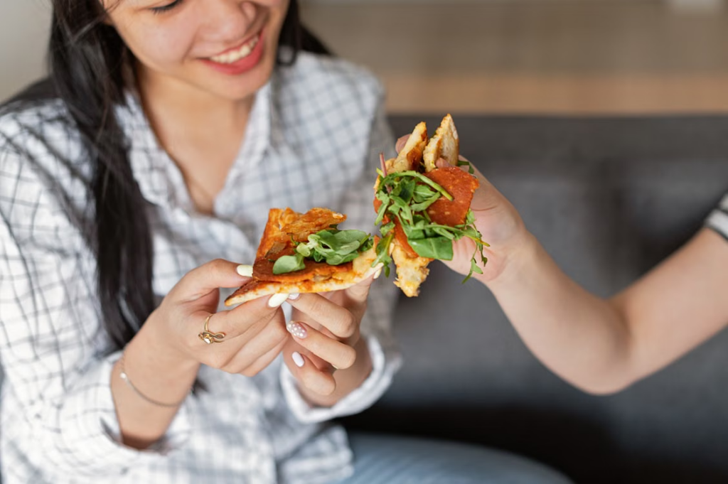 A woman smiles while eating pizza.