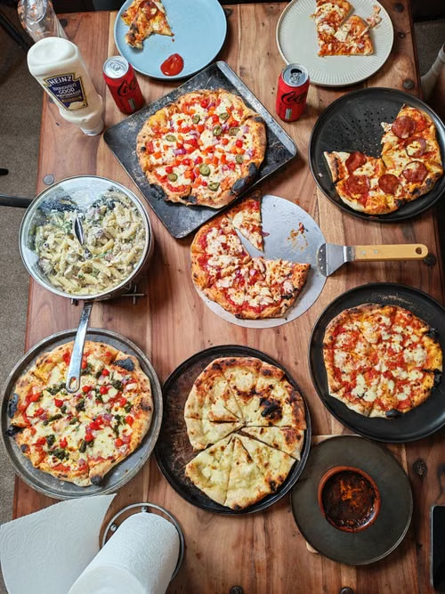 Table filled with assorted pizzas, pasta dishes, and beverages